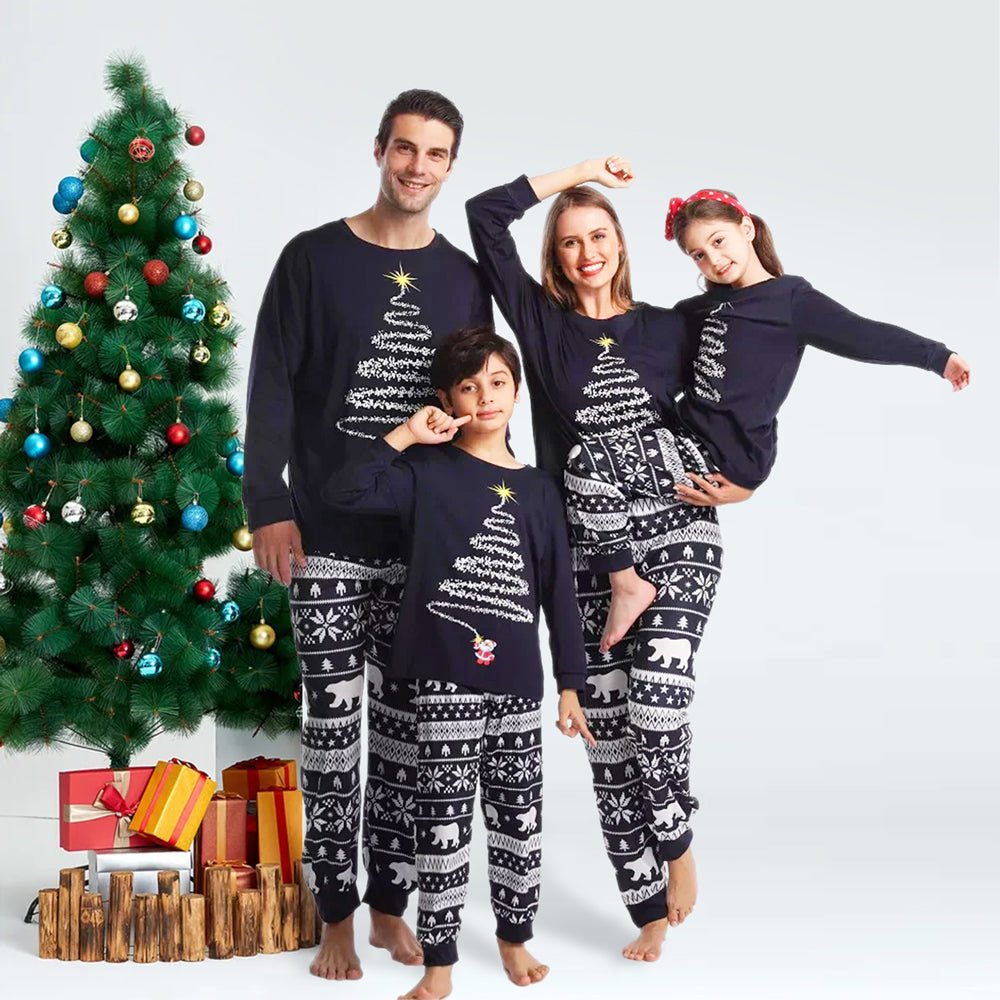 Familia junto a un árbol y regalos con camisetas de pijama azul marino con dibujo de árbol de Navidad y pantalones azul marino y blancos con estampado de osos polares.
