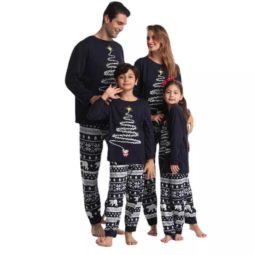 Padres y dos niños de pie juntos con camisetas de pijama azul marino con árboles de Navidad y pantalones azul marino y blancos con estampado de osos polares.