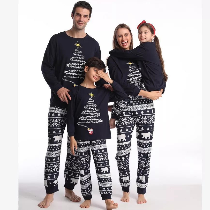 Padres con dos niños posando con camisetas de pijama azul marino con dibujo de árbol de Navidad y pantalones azul marino y blancos con estampado de osos polares.