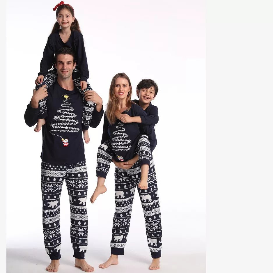 Padres llevando en brazos a dos niños con camisetas de pijama azul marino con árboles de Navidad y pantalones azul marino y blancos con estampado de osos polares sobre fondo blanco.