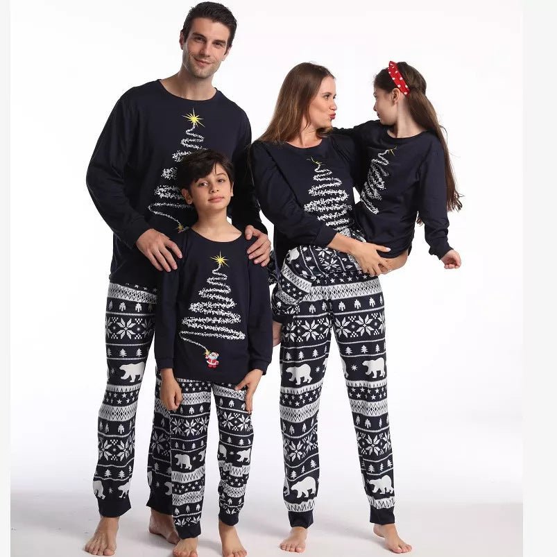 Madre sujetando a su hija junto al padre y el hijo con camisetas azul marino con dibujo de árbol y pantalones de pijama con estampado de osos polares.