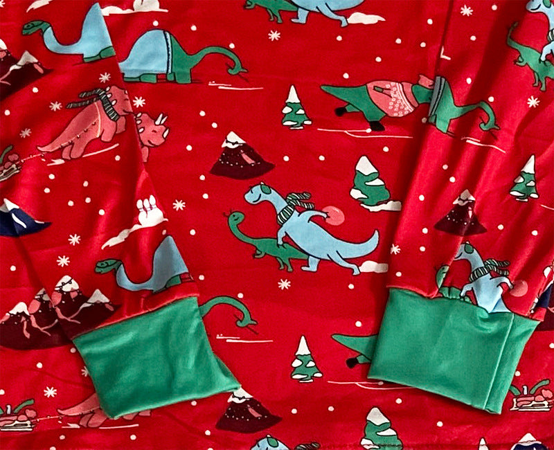 Close-up of green sleeve cuffs on red Christmas pajamas printed with colorful dinosaurs, snowy mountains and trees.